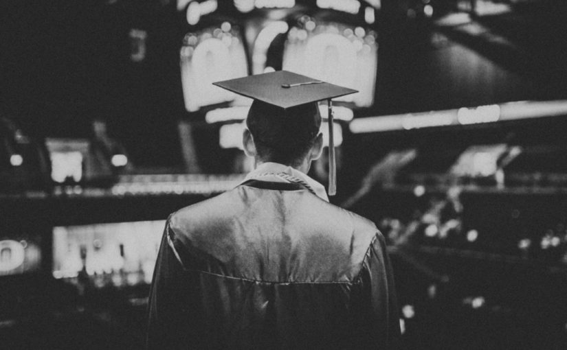 Black and white photo of a graduate's back, looking toward an arena's crowd