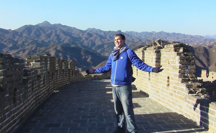Christopher Wink in blue jacket with arms spread wide on the Great Wall of China